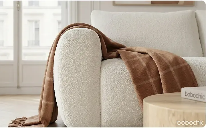 Cremefarbenes Sofa mit karamellfarbenem Plaid und hellem Beistelltisch im Fensterlicht – Bobochic Paris