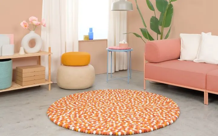 Runder Filzkugelteppich Juna in Orange und Weiß vor einem apricotfarbenen Sofa – myfelt