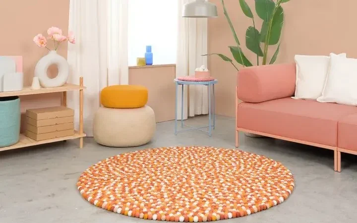 Runder Filzkugelteppich Juna in Orange und Weiß vor einem apricotfarbenen Sofa – myfelt