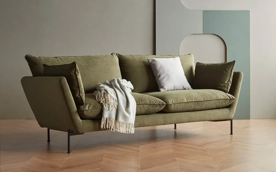 Olivgrünes Sofa Anton mit Kissen und heller Decke auf einem Holzboden – Skandi Home